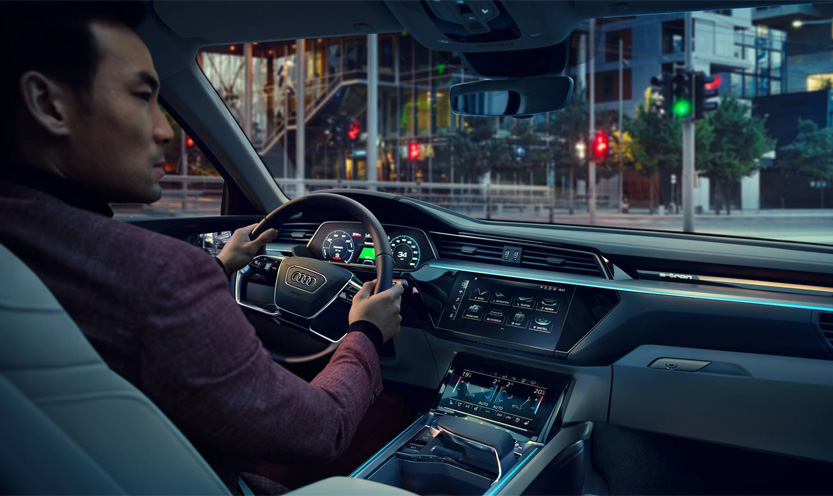 Une personne assise sur le siège conducteur d'un véhicule Audi, utilisant l'écran MMI.