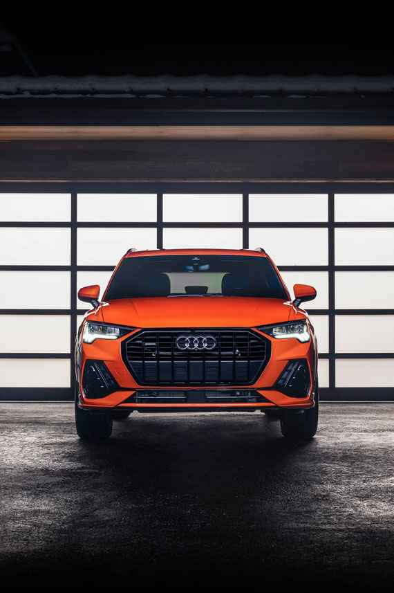 Front profile of an orange Audi Q3 parked in front of a lit up residential garage.