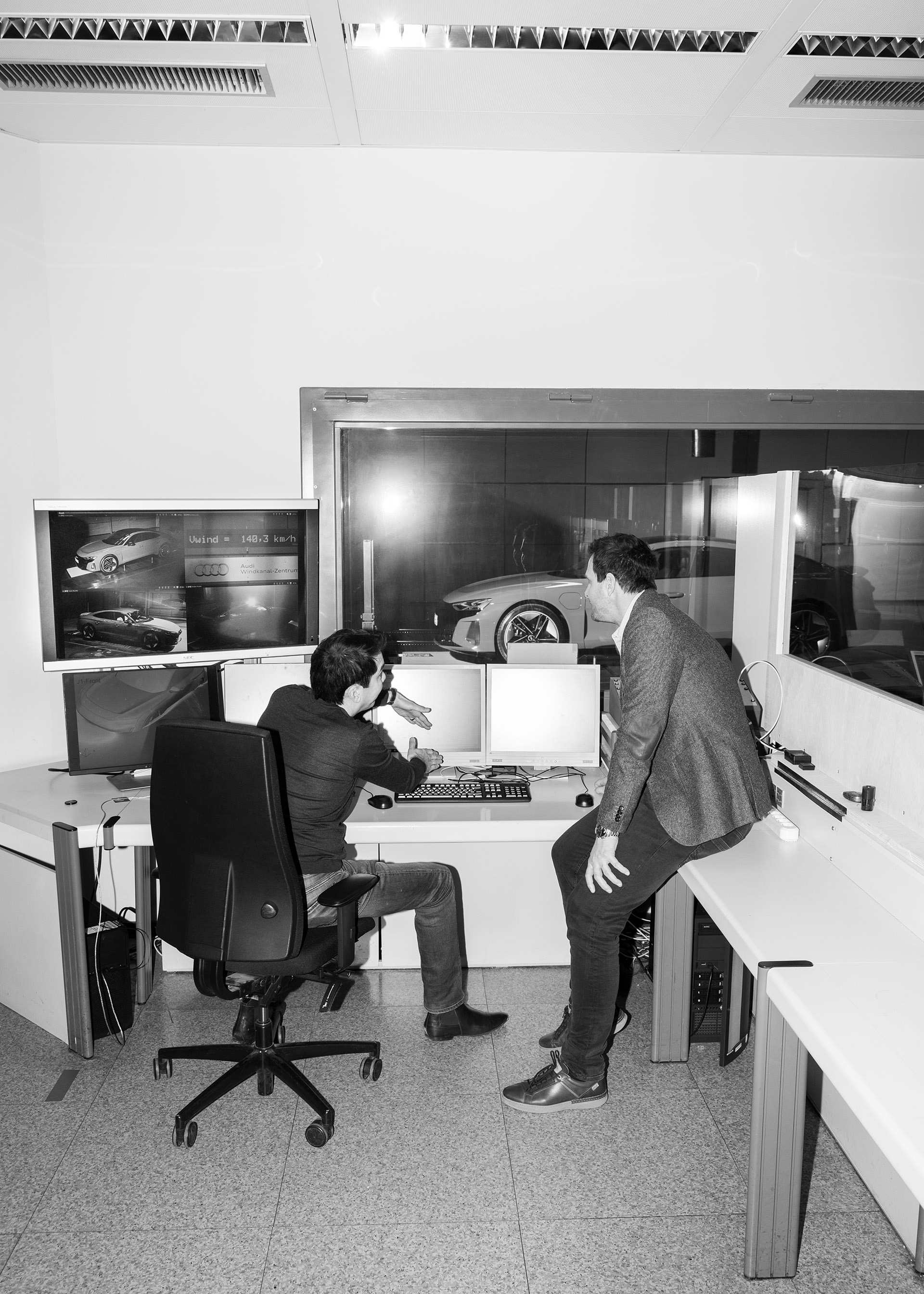 Dr. Kentaro Zens and Thomas Redenbach discuss the RS e-tron GT in front of a computer in the observation room at the Audi aerodynamics testing facility.