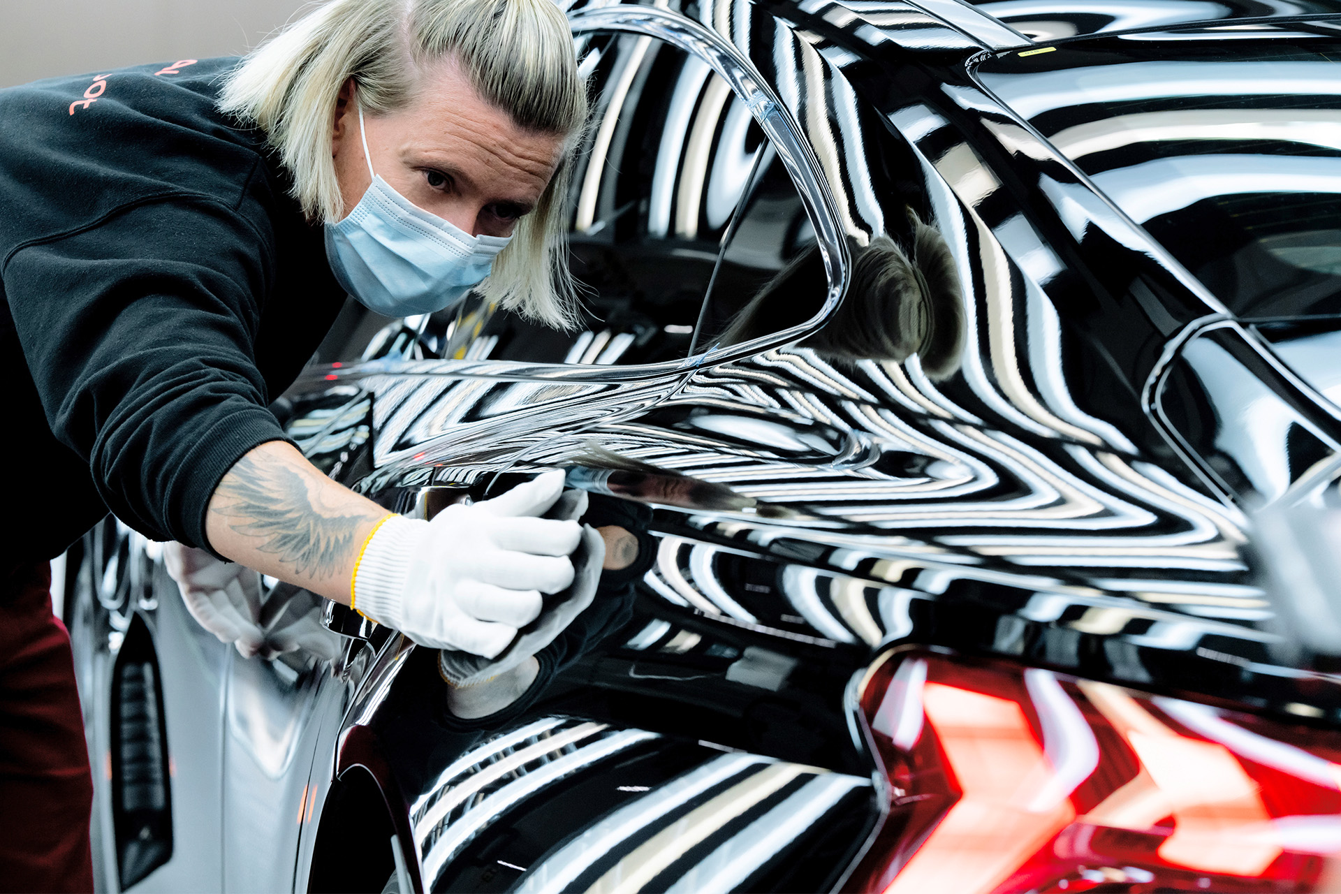 Un technicien Audi passe une main gantée sur une Audi e-tron GT nouvellement construite pour la dernière vérification de la qualité de la peinture.